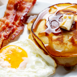 Pancakes covered in syrup, egg, and bacon