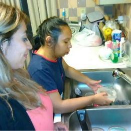 Young lady washing dishes at home with supervision